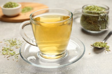 Photo of Aromatic fennel tea and seeds on light grey table, closeup