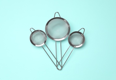 Photo of Different skimmers on turquoise background, flat lay. Cooking utensils