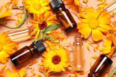 Bottles of essential oils and beautiful calendula flowers on beige background, flat lay