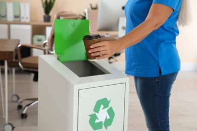 Photo of Woman throwing coffee cup into recycling bin at office, closeup