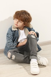 Photo of Fashion concept. Stylish boy sitting near white wall
