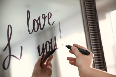 Photo of Woman writing romantic message I Love You on mirror in room, closeup