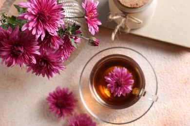 Beautiful chrysanthemum flowers and cup of tea on beige textured table, above view