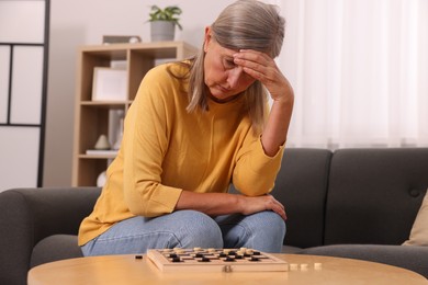 Thoughtful senior woman playing checkers at home