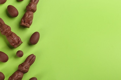 Photo of Flat lay composition with chocolate Easter bunnies and eggs on green background. Space for text