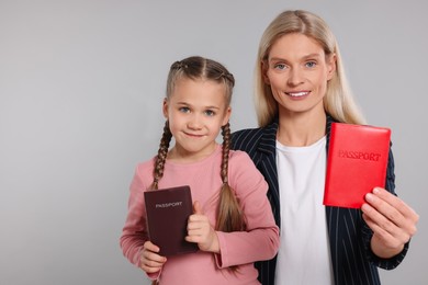 Immigration. Happy woman and her daughter with passports on gray background, space for text