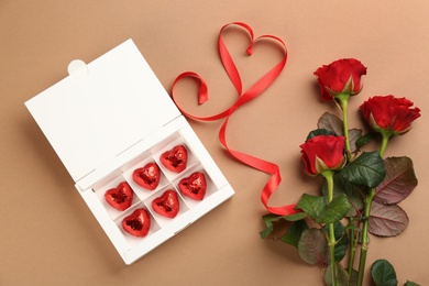 Photo of Box of heart shaped chocolate candies and bouquet on brown background, flat lay