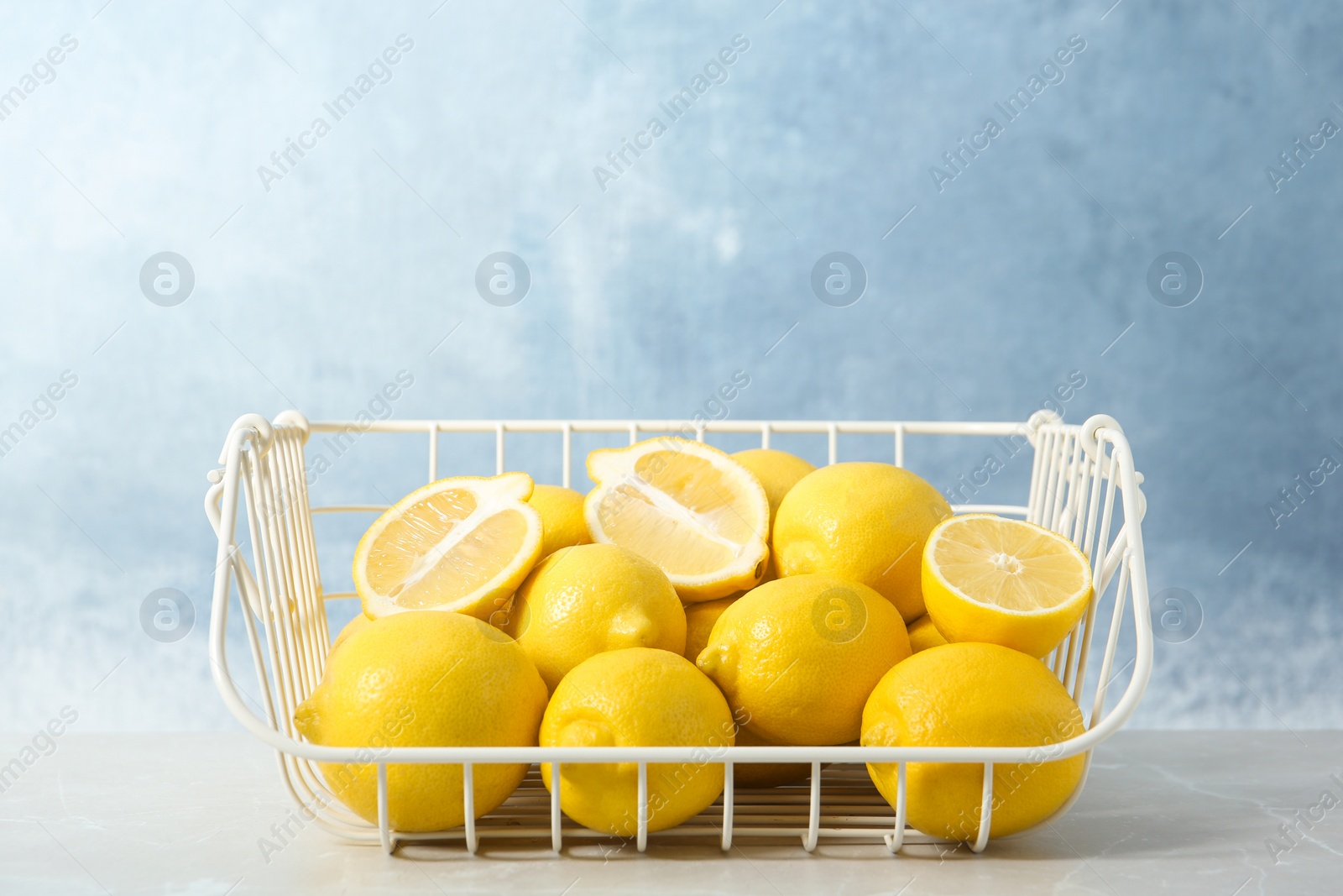 Photo of Wire basket with lemons on table against color background