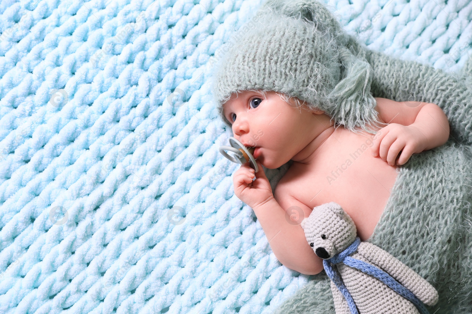 Photo of Cute newborn baby with pacifier and crochet toy on light blue blanket, top view. Space for text