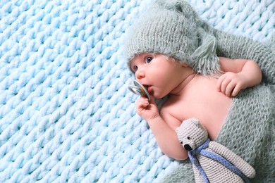 Cute newborn baby with pacifier and crochet toy on light blue blanket, top view. Space for text