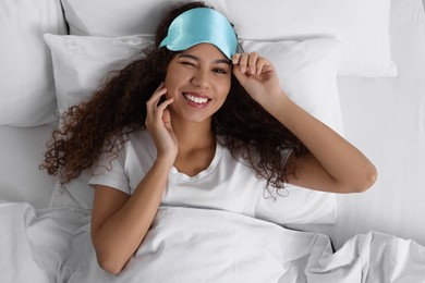Happy African American woman with sleeping mask in bed, top view