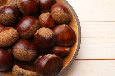 Photo of Sweet fresh edible chestnuts on light wooden table, top view. Space for text