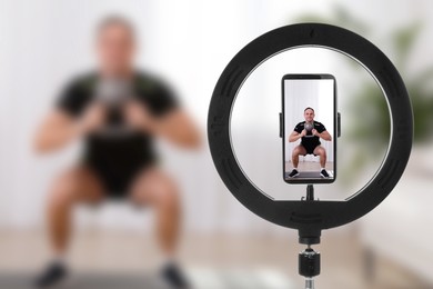 Image of Muscular man training with kettlebell at home, selective focus on ring light and smartphone display