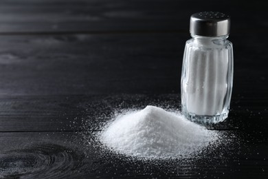 Photo of Organic salt in glass shaker on black wooden table, closeup. Space for text