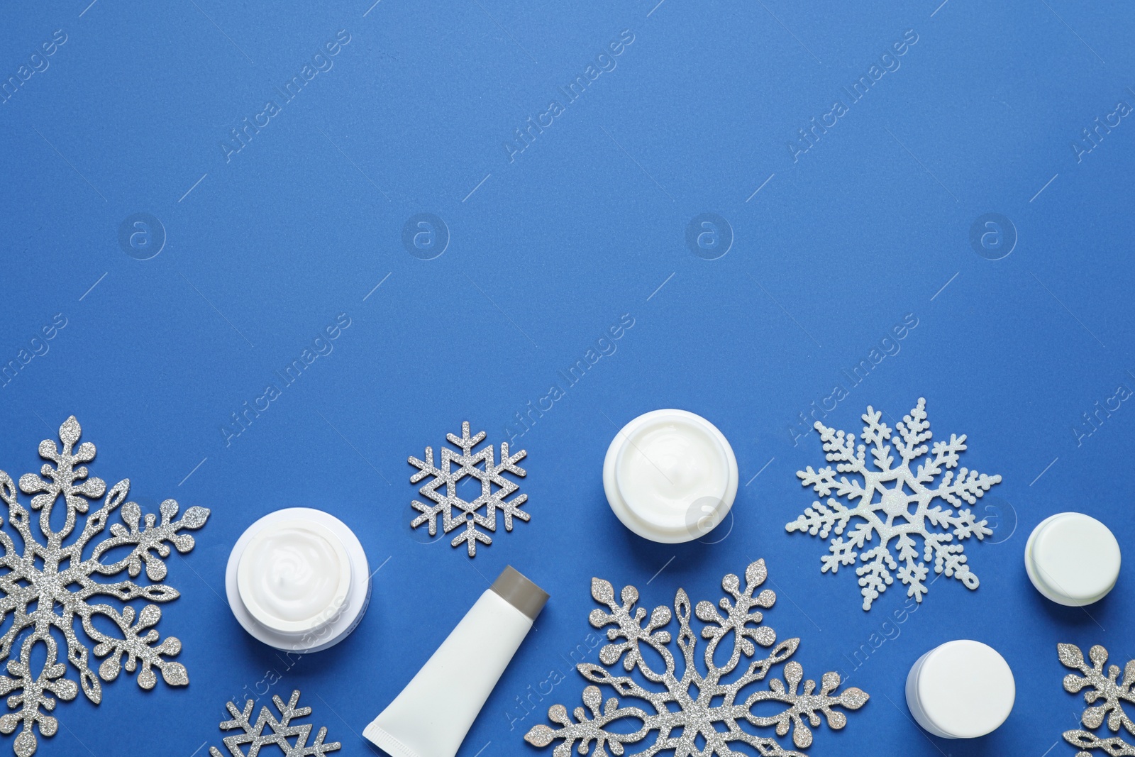 Photo of Flat lay composition with cosmetic products and snowflakes on blue background, space for text. Winter skin care