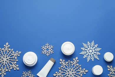 Photo of Flat lay composition with cosmetic products and snowflakes on blue background, space for text. Winter skin care