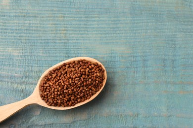 Photo of Spoon with buckwheat tea granules on light blue wooden table, top view. Space for text