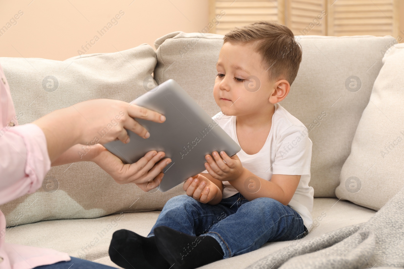 Photo of Internet addiction. Mother taking away tablet from her little son on sofa at home, closeup