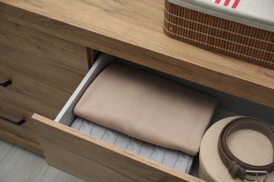 Photo of Chest of drawers with different folded clothes and accessories indoors, closeup