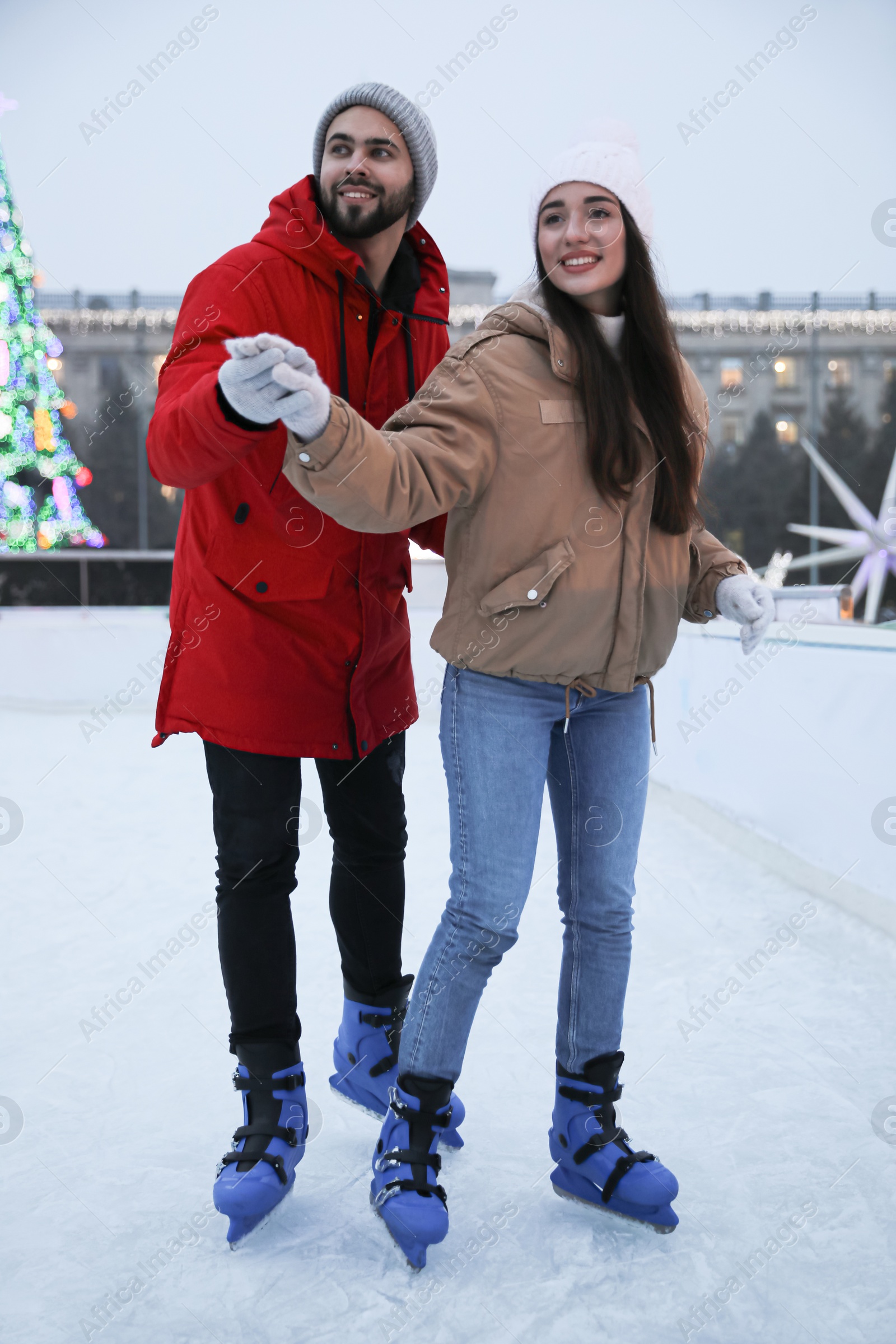 Image of Happy young couple skating at outdoor ice rink