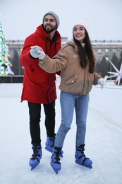 Image of Happy young couple skating at outdoor ice rink
