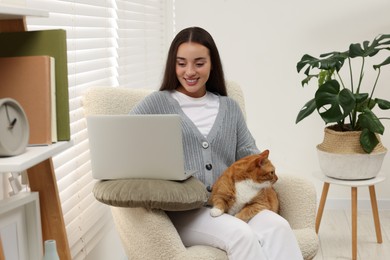 Photo of Happy woman working with laptop and petting cute cat at home