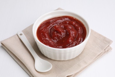 Photo of Organic ketchup in bowl and spoon on white table. Tomato sauce