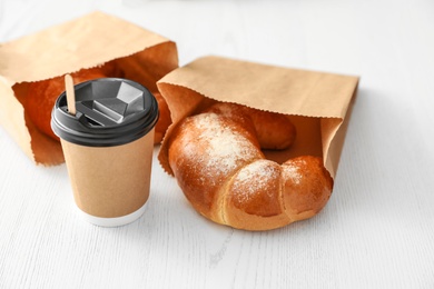 Photo of Cup of coffee and pastry in paper bags on wooden table