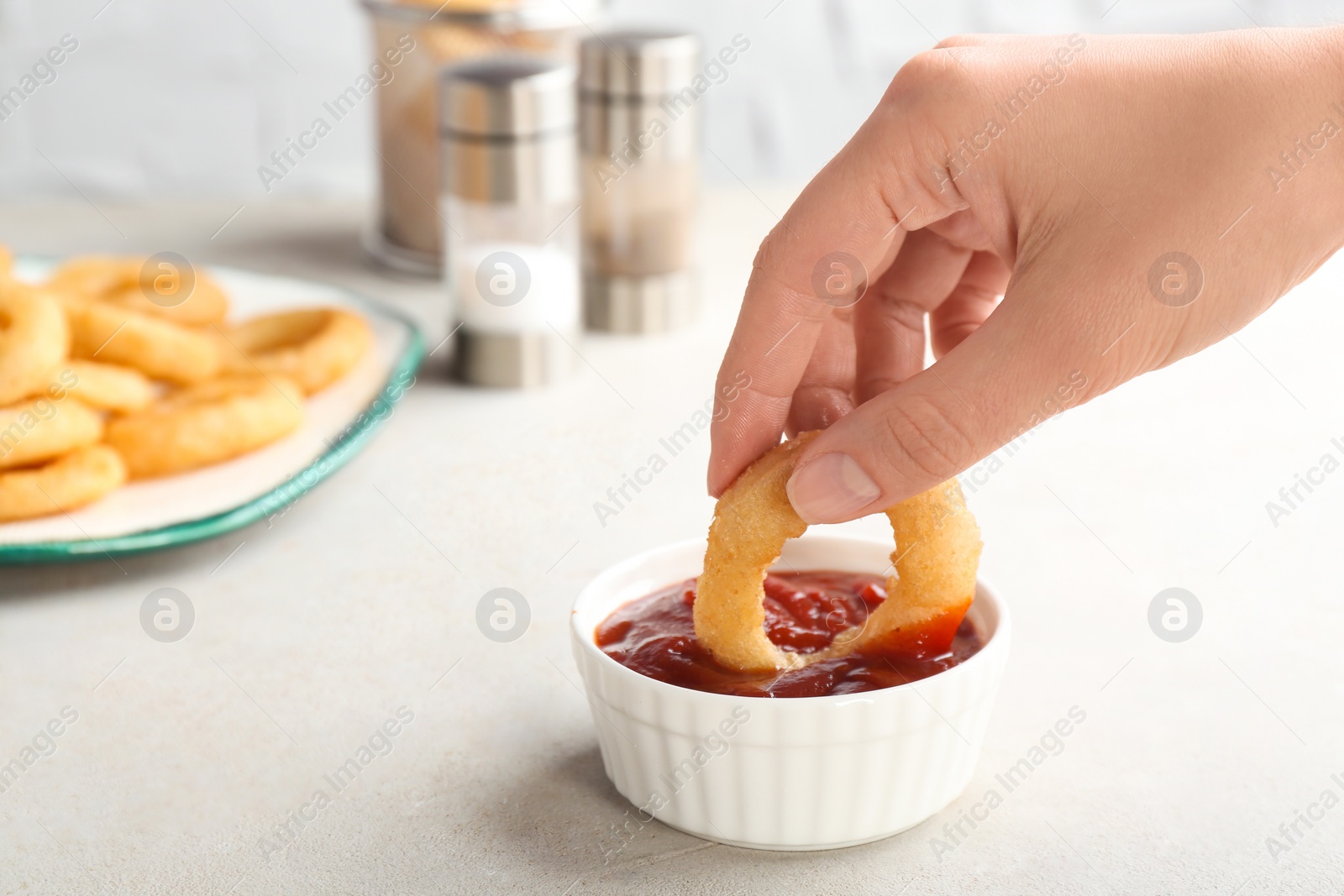 Photo of Woman dipping tasty onion ring into bowl with ketchup on table