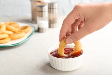 Photo of Woman dipping tasty onion ring into bowl with ketchup on table