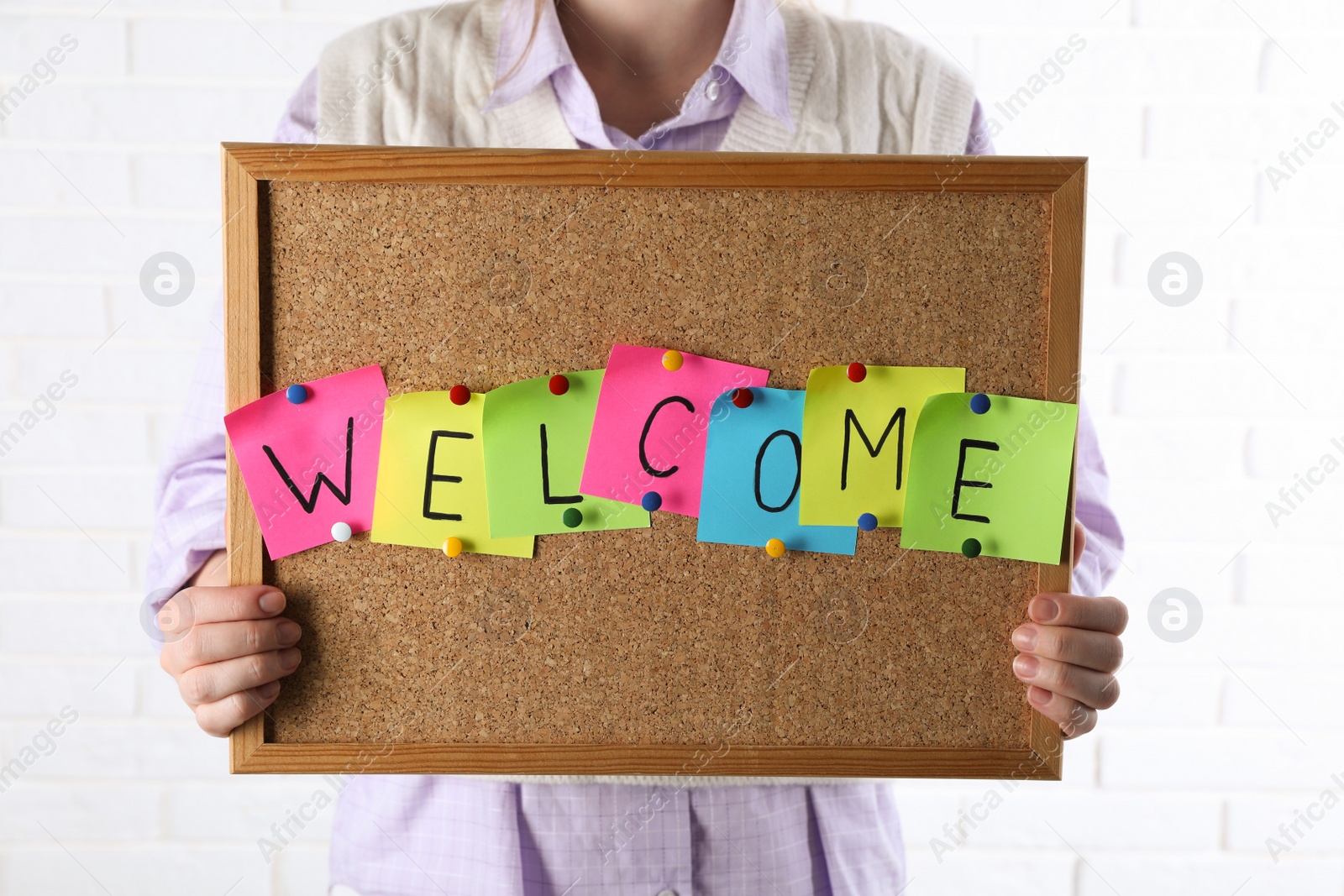 Photo of Woman holding corkboard with word Welcome near white brick wall, closeup