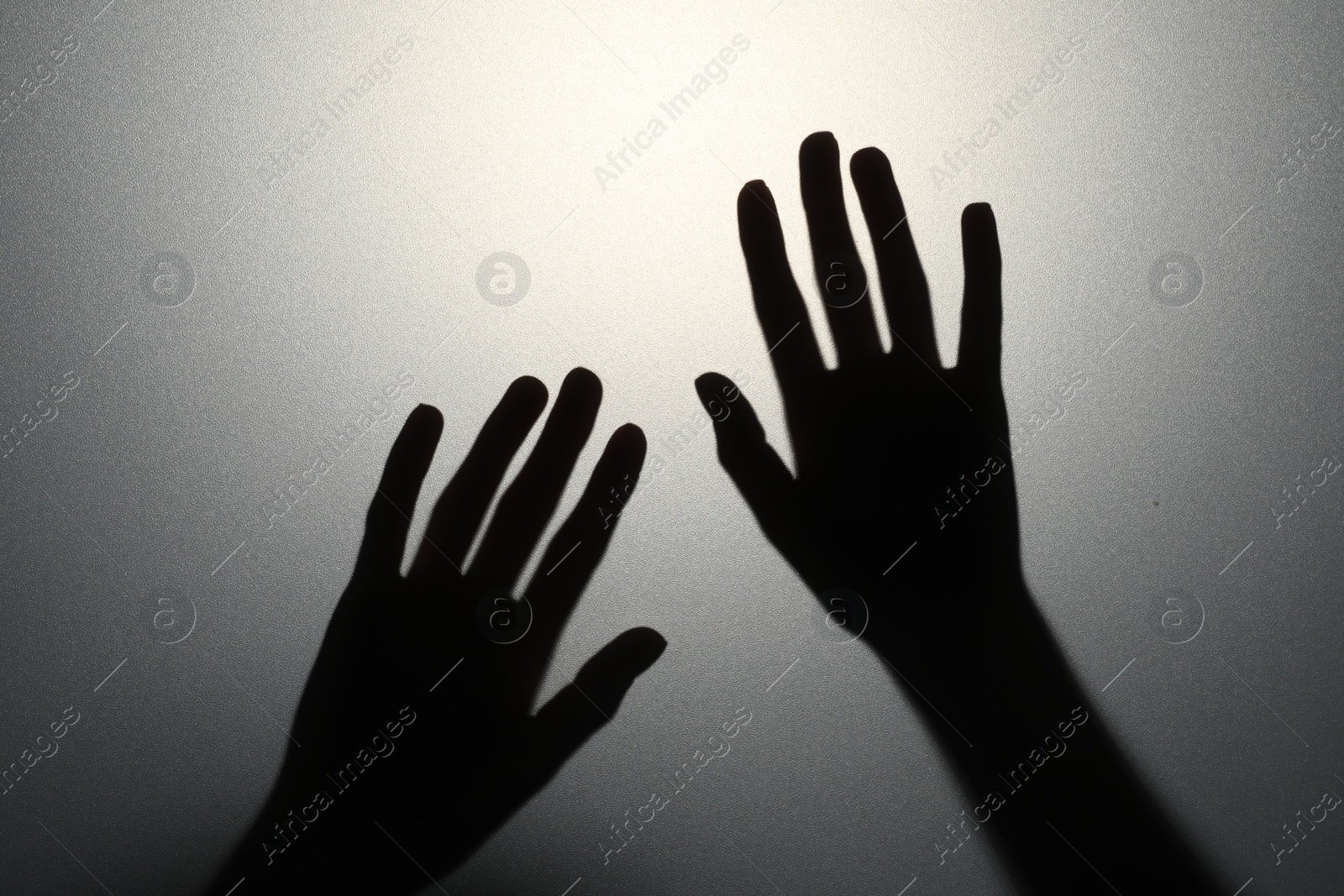 Photo of Silhouette of creepy ghost behind glass against grey background, closeup