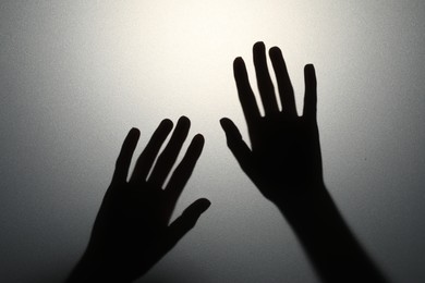 Photo of Silhouette of creepy ghost behind glass against grey background, closeup