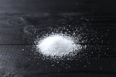 Photo of Pile of organic salt on black wooden table, closeup