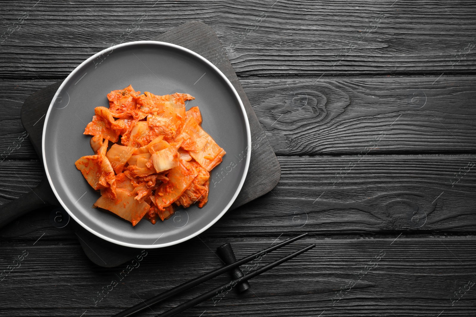 Photo of Delicious kimchi with Chinese cabbage served on black wooden table, flat lay. Space for text