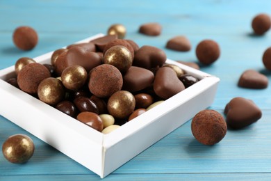 Photo of Different delicious chocolate candies in box on light blue wooden table, closeup