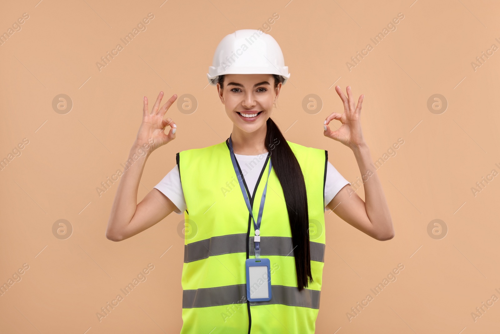 Photo of Engineer with hard hat and badge showing ok gesture on beige background