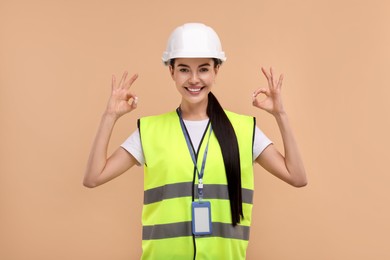 Engineer with hard hat and badge showing ok gesture on beige background