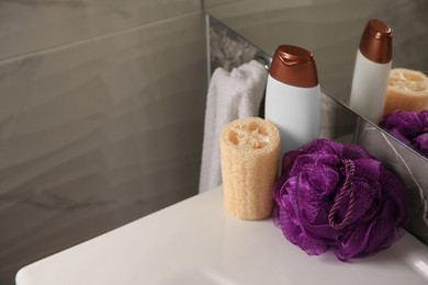 Photo of Purple shower puff, loofah sponge and bottle of body wash gel on sink in bathroom, space for text