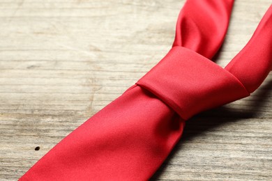 Photo of One red necktie on light wooden table, closeup