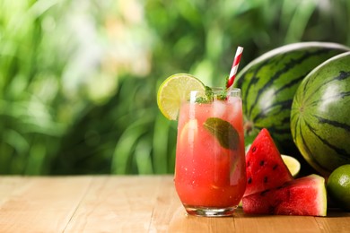 Glass of freshly made watermelon juice with lime and mint on wooden table outdoors, space for text