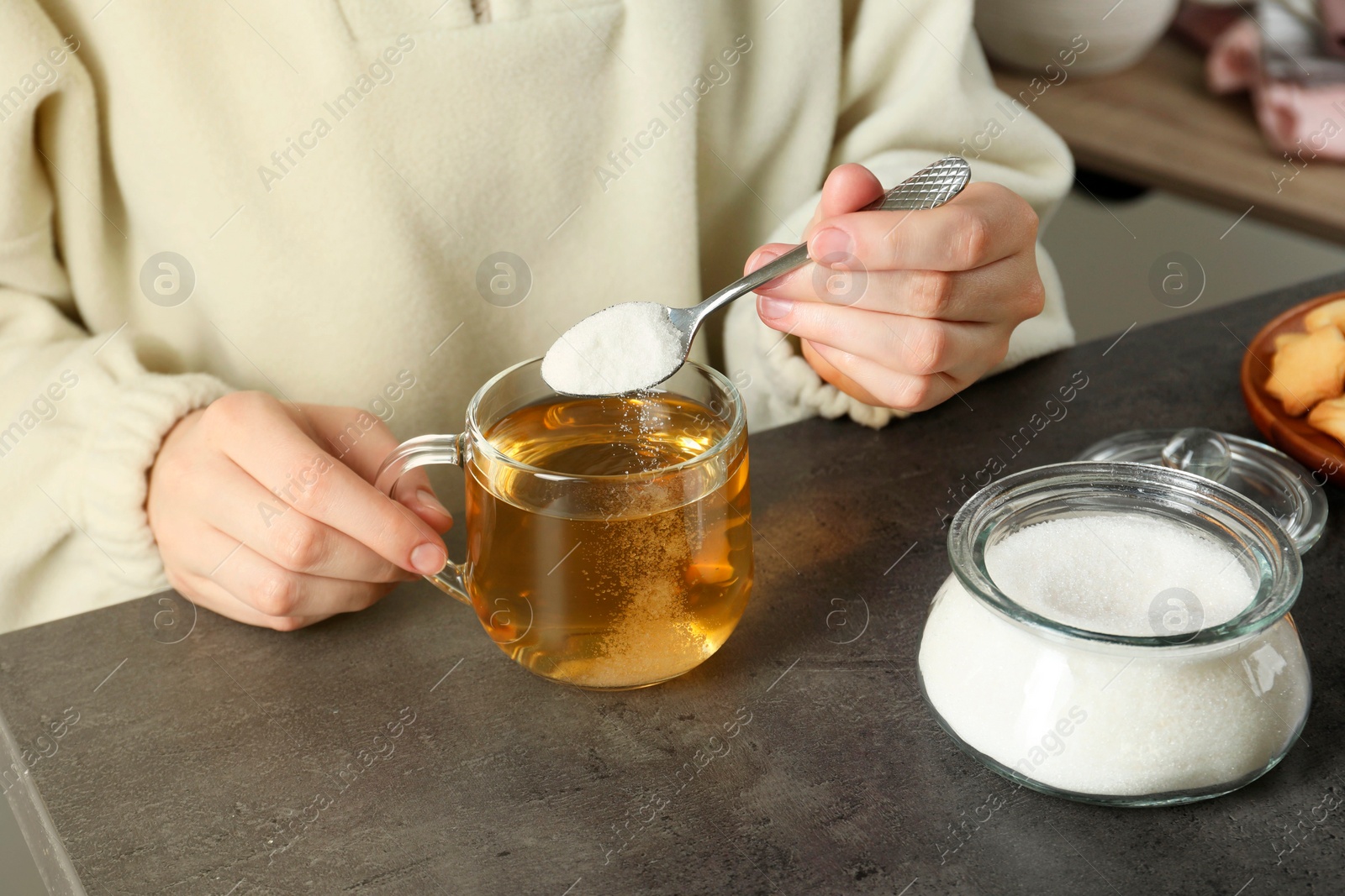 Photo of Woman adding sugar into aromatic tea at grey table, closeup