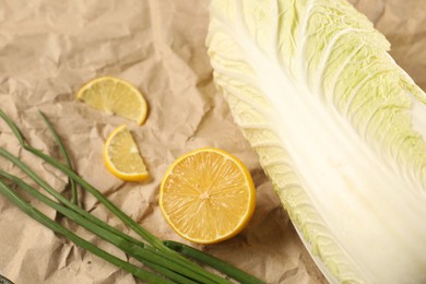 Photo of Fresh Chinese cabbage, lemon and green onion on kraft paper, closeup