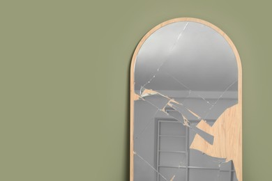 Photo of Broken mirror with many cracks near olive wall indoors. Space for text