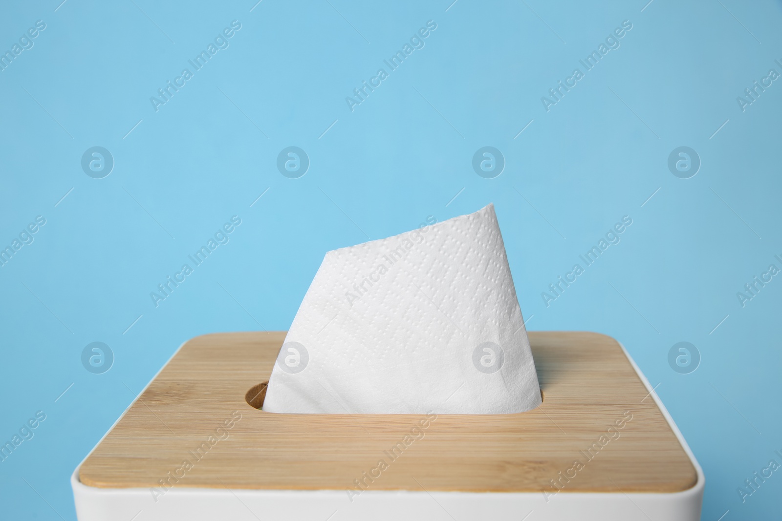 Photo of Holder with paper tissues on light blue background, closeup