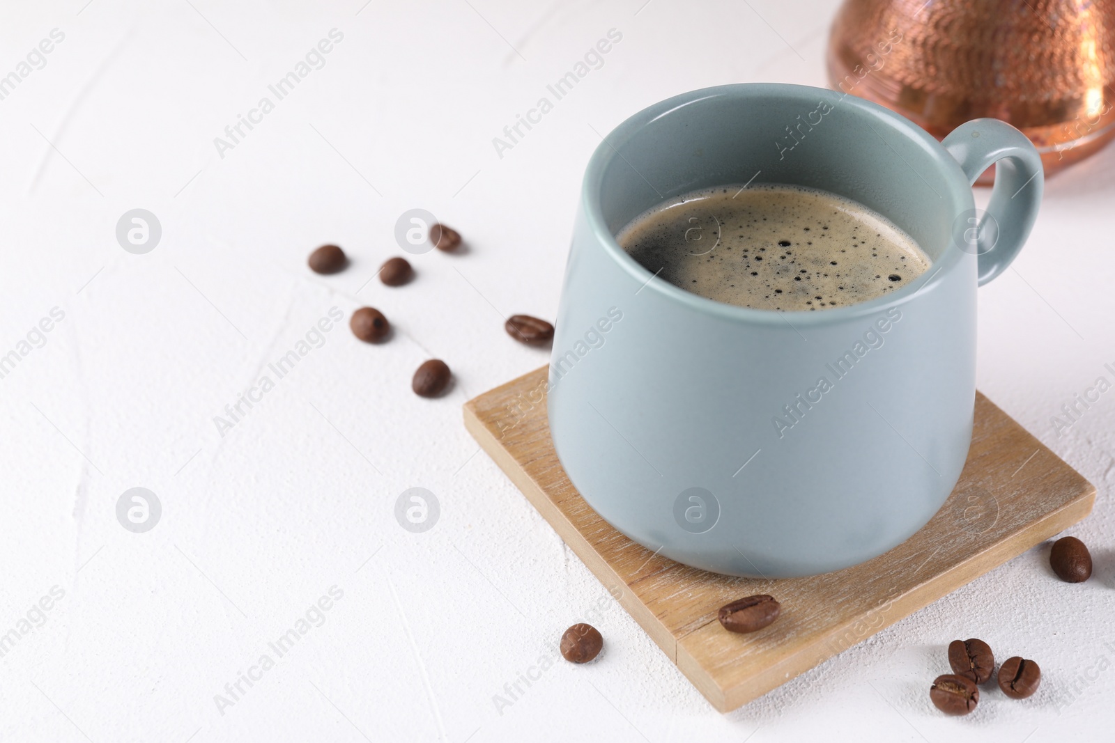 Photo of Delicious coffee in cup and beans on white textured table, closeup. Space for text