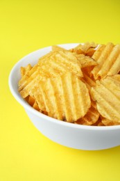 Bowl of tasty ridged potato chips on yellow background, closeup