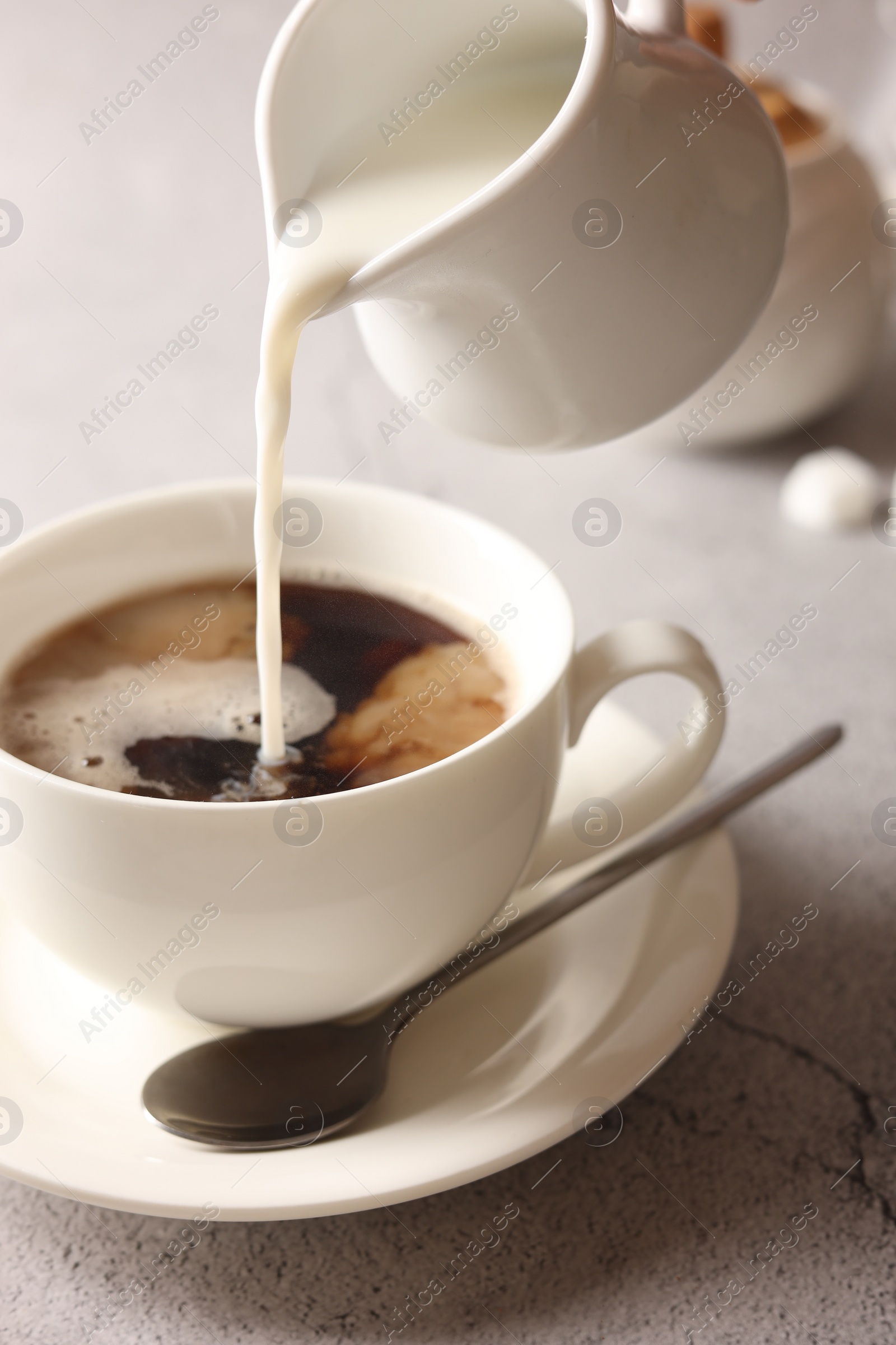 Photo of Pouring milk into cup with coffee on light grey textured table, closeup