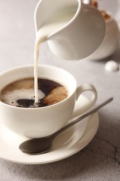 Pouring milk into cup with coffee on light grey textured table, closeup