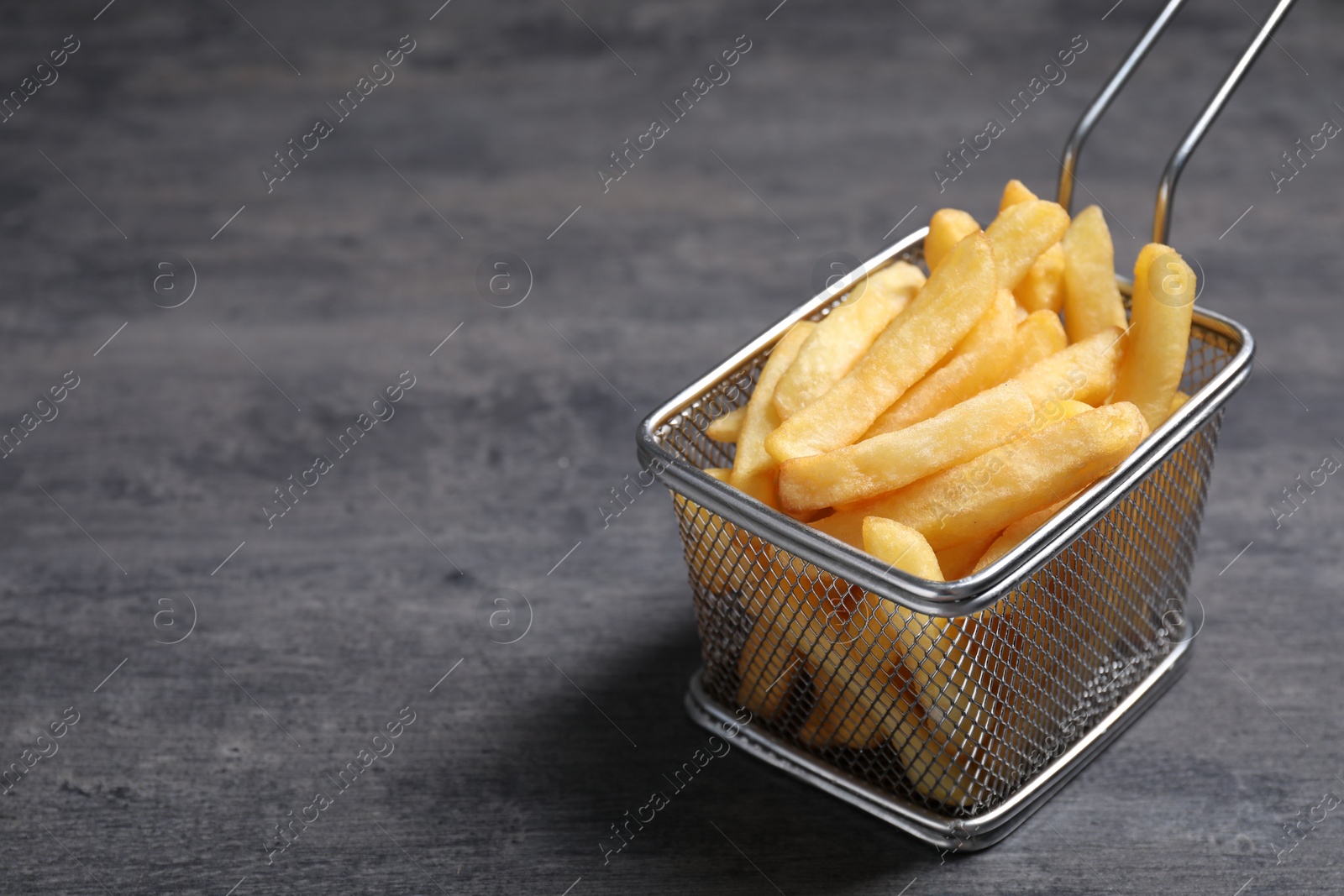 Photo of Metal basket with tasty French fries on grey table, closeup. Space for text